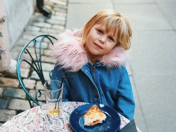 Portrait of smiling cute girl with food plate on table sitting at sidewalk cafe