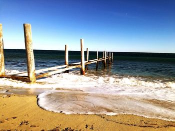 Wooden posts on beach against clear blue sky