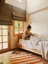 Young woman reading book while sitting on bed at home