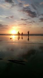 Silhouette friends standing at beach against sky during sunset