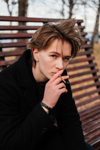 Portrait of young man smoking cigarette while sitting outdoors