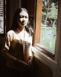 Portrait of woman standing by window at home