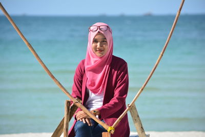 Portrait of smiling woman wearing pink hijab sitting at beach