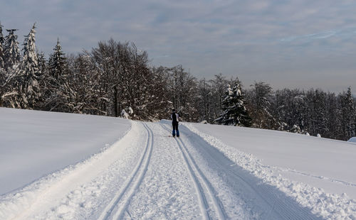 Man walking on snow covered field against sky