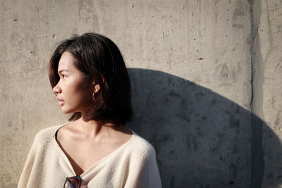 Portrait of young woman looking away against wall