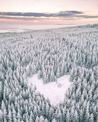 Aerial view of heart shape on snow covered land amidst trees against sky during sunset