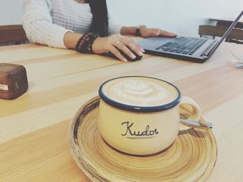 Midsection of woman using laptop by coffee served on table at cafe