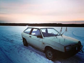 Snow covered car against sky during sunset