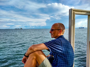 Man sitting in sea against sky