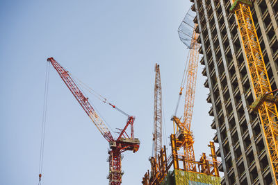 Low angle view of cranes on construction site against clear sky