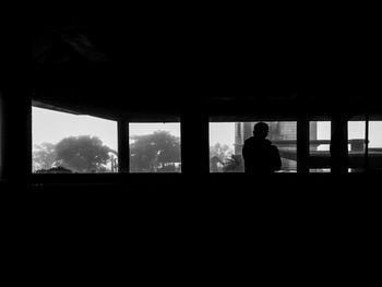 Silhouette man looking through window