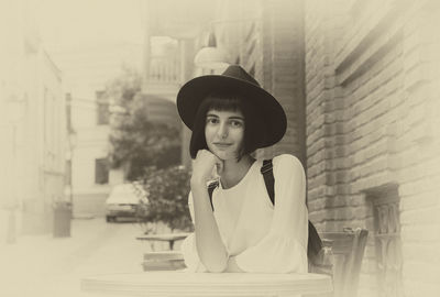 Portrait of young woman wearing hat while sitting at sidewalk cafe
