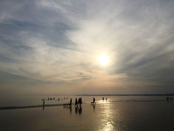 Silhouette people on beach against sky during sunset