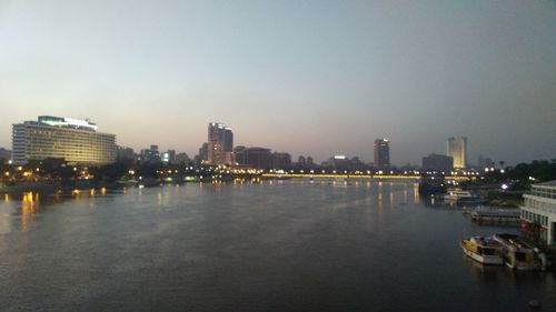 Illuminated buildings by river against sky in city