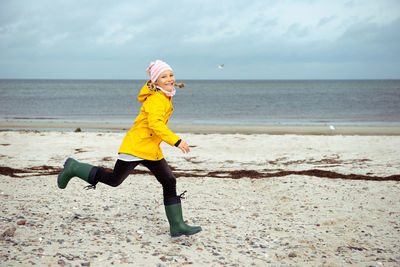 Side view of smiling girl running at beach against sky