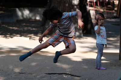 Full length of boy jumping while girl standing in background at playground