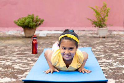 An indian girl child practicing yoga in smiling face on yoga mat outdoors