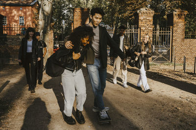 Smiling male and female friends walking in park during sunny day