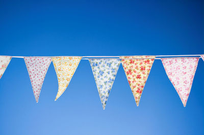 Low angle view of bunting flags hanging against clear blue sky