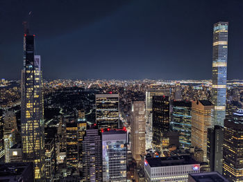 Illuminated modern buildings in city against sky at night