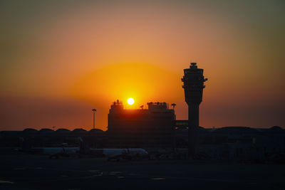 Silhouette factory against orange sky