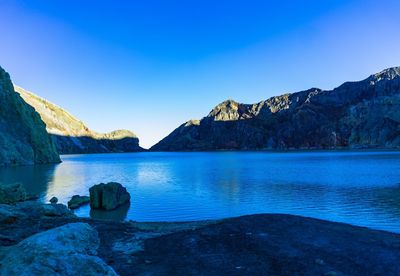 Scenic view of sea and mountains against clear blue sky