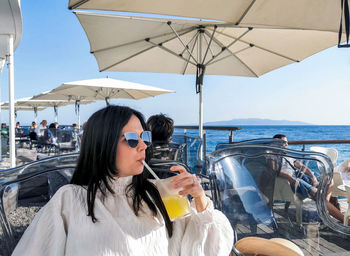 Portrait of beautiful and stylish young woman drinking cold drink in bar on sea shore.