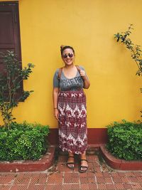 Portrait of smiling young woman standing against yellow wall