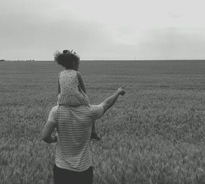Rear view of father carrying daughter on shoulder at field