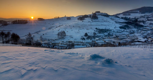 Snow covered landscape against sky during sunset