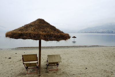 Empty chairs with thatched roof at beach against sky