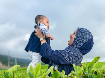 Side view of mother holding baby against sky