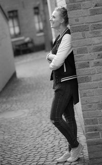 Side view of young woman leaning on brick wall in city