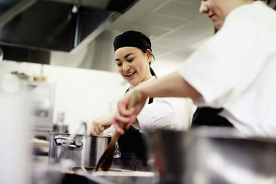 Smiling female chef student with colleague cooking food in commercial kitchen