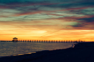 Silhouette pier on beach against sky during sunset