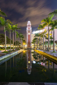Clock tower reflecting in pond amidst palm trees at night