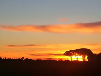 Silhouette trees on field against romantic sky at sunset