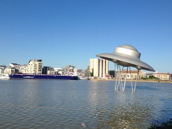 Buildings by sea against clear blue sky