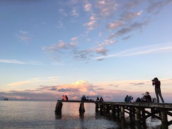 People on pier by sea against sky during sunset