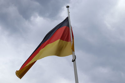 Germany flag at a flagpole moving in the wind against the sky