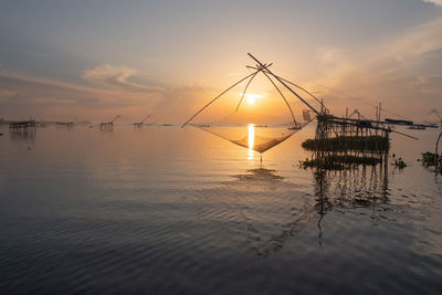 Silhouette fishing net on shore against sky during sunset