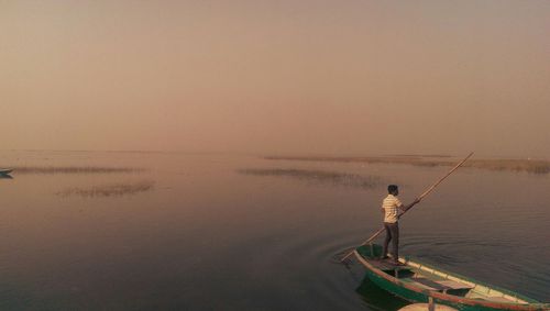 Man on boat in sea against sky during sunset