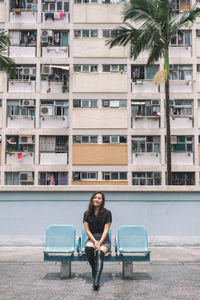 Full length portrait of woman sitting against building in city