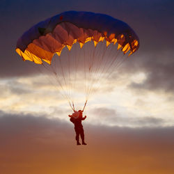 Low angle view of man paragliding against sky during sunset