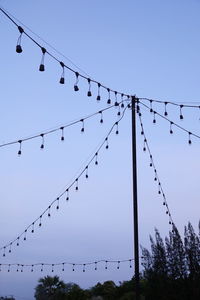 Low angle view of birds perching on cable against sky