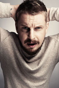 Portrait of bearded man with hands behind head against gray background