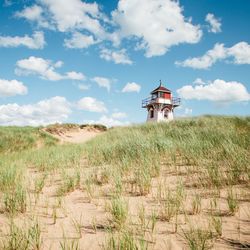 Lighthouse on field against cloudy sky