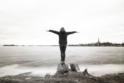 Rear view full length of woman with arms outstretched standing by frozen lake