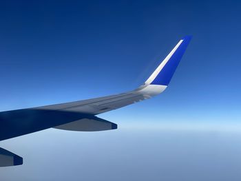 Cropped image of airplane wing against blue sky