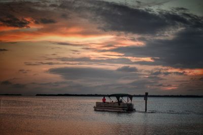 People sailing boat in sea against sky during sunset